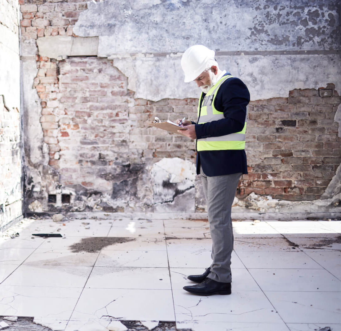 Property appraiser looking down at clipboard while standing inside a damaged building