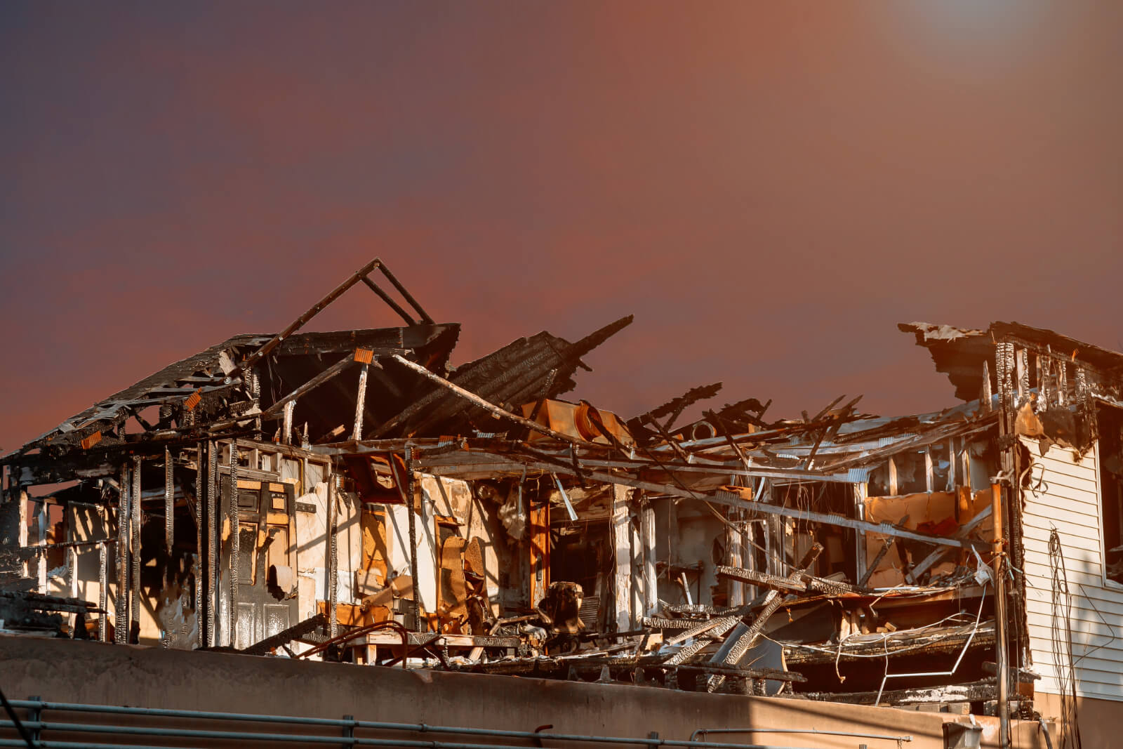 Burnt home destroyed by fire in front of a dark, hazy sky